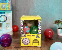 Sugoi Mart mini yellow colored gachapon box with grey background.